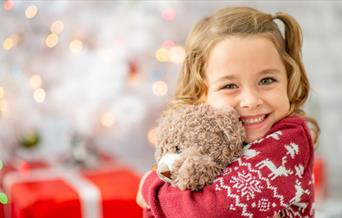 Happy preschool child cuddling teddy bear and wearing a Christmas jumper
