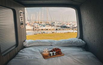 Camper van from Waterside Campers, with double bed opening to view over marina and breakfast tray with croissants and orange juice