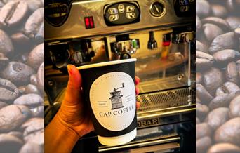 Takeaway cup with Cap Coffee logo on, with background of coffee beans