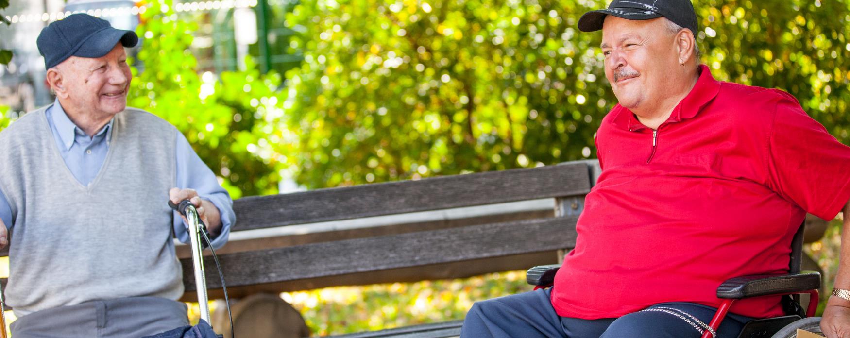 Older men chatting on bench, one in wheelchair