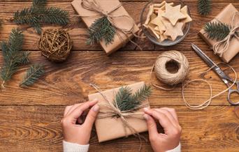 Christmas present being wrapped with eco-wrapping paper, string and natural foliage