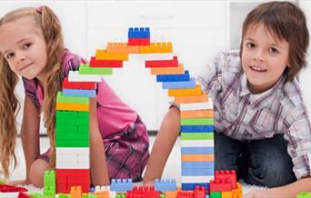 A boy and girl building a bridge with coloured blocks