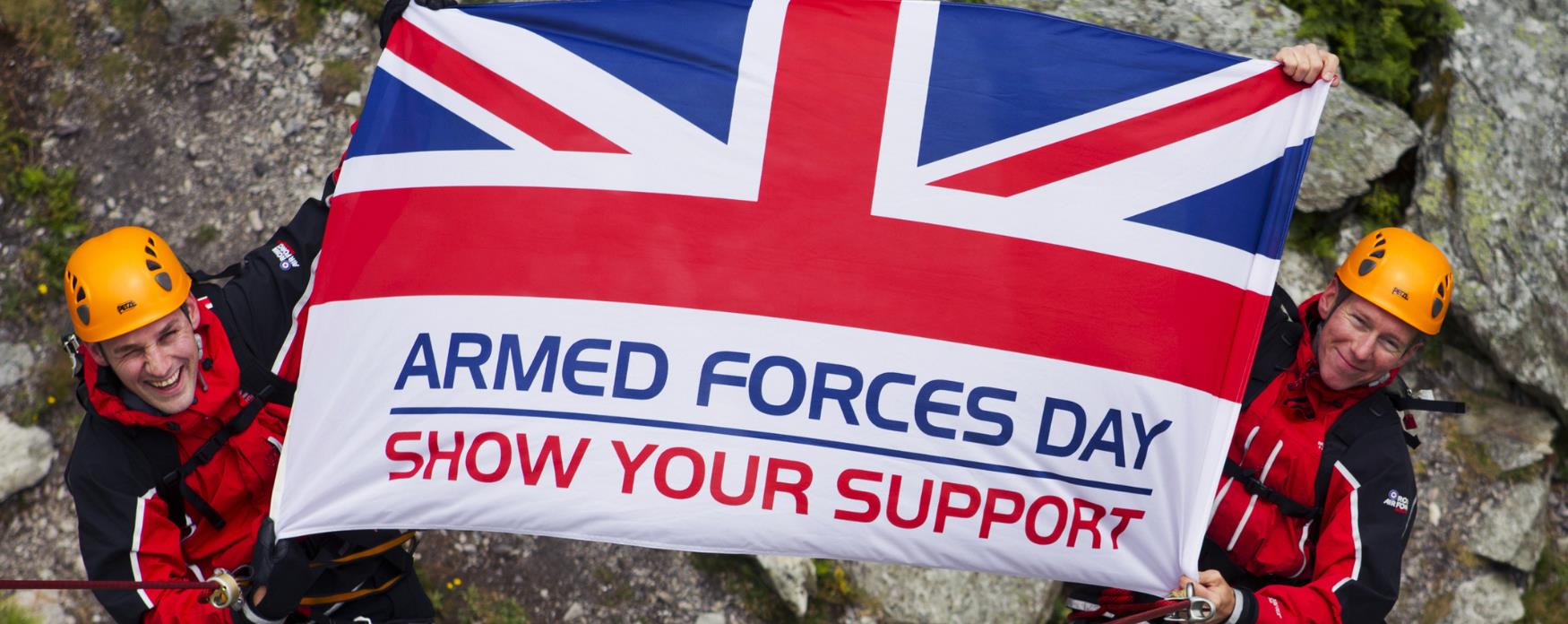Soldiers abseiling down cliff holding banner for Armed Forces Day