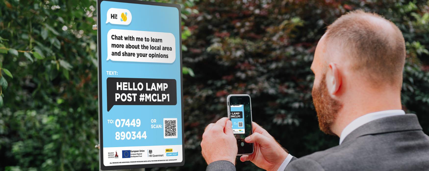 Man in suit pointing smart phone at poster explaining Hello Lamp Post