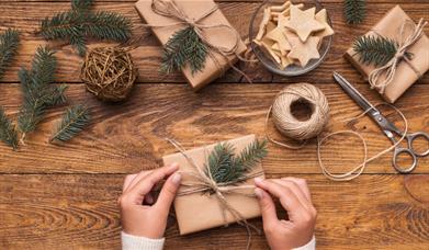 Christmas present being wrapped with eco-wrapping paper, string and natural foliage