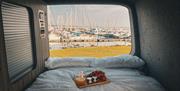 Camper van from Waterside Campers, with double bed opening to view over marina and breakfast tray with croissants and orange juice