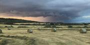 Fields at Blue House Farm with storm clouds gathering overhead and large round bales