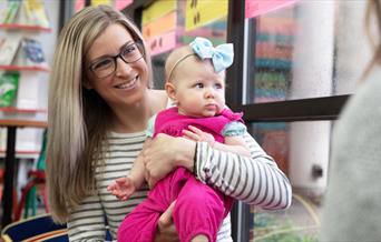 Mother in library with baby wearing cute headband and pink outfit