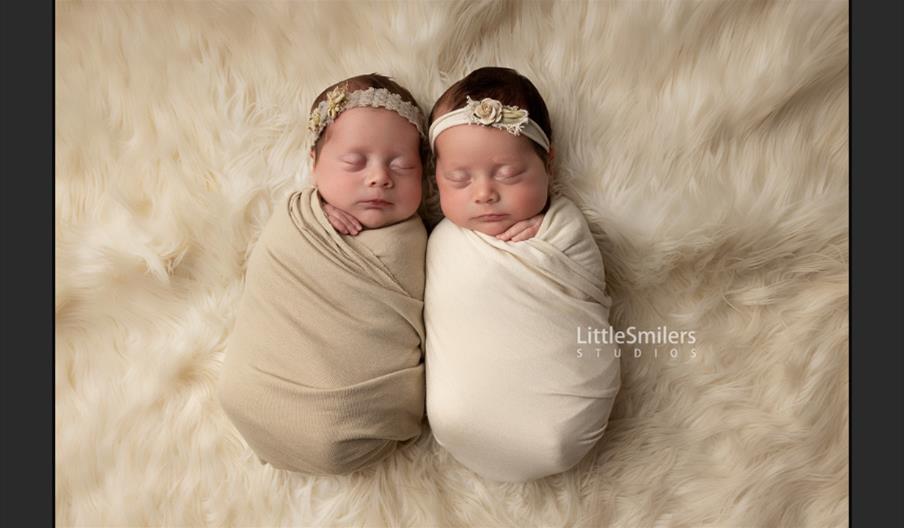 Beautiful newborn photoshoot of twin babies wrapped up in swaddling and wearing headbands, by Little Smilers