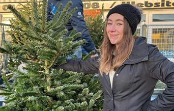 Young woman in bobble hat holding Christmas tree at Maldon Young Farmers tree sale