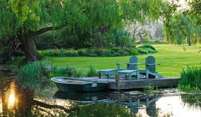 Country garden with pond, rowing boat and wooden deck chairs