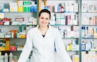 Pharmacy assistant in front of shelves of assorted medicine