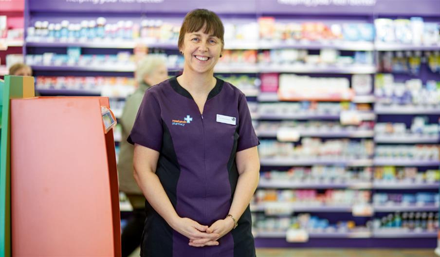Pharmacy assistant smiling in front of shelves of medicines