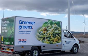 Electric Tesco delivery van in front of wind farm