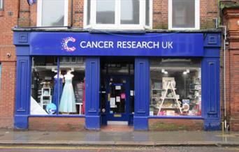 Outside of Cancer Research charity shop in Maldon High Street with cheery blue paintwork and long dresses in the window