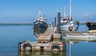 Boats moored on a wooden pontoon with deep blue sky and sea, Maylandsea