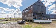 Black weatherboarded boat builders workshop with boats surrounding it