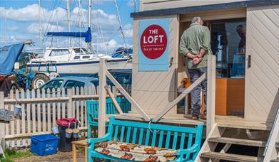 Outside of The Loft Tea by the Sea with blue bench seat and boats in the background