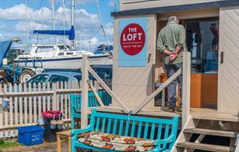 Outside of The Loft Tea by the Sea with blue bench seat and boats in the background