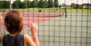 A young girl looking through the fence of the tennis courts