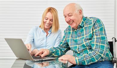 A younger woman teaching an older man to use a laptop computer
