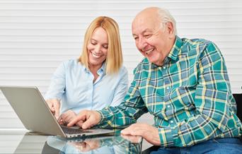 A younger woman teaching an older man to use a laptop computer