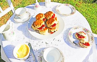 A cream tea lunch of scones and cups of tea placed on a table in an outdoor area
