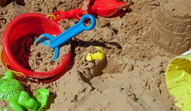 A sand pit strewn with beach toys