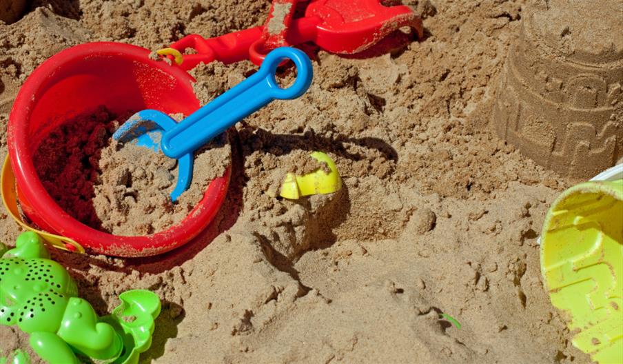 A sand pit strewn with beach toys